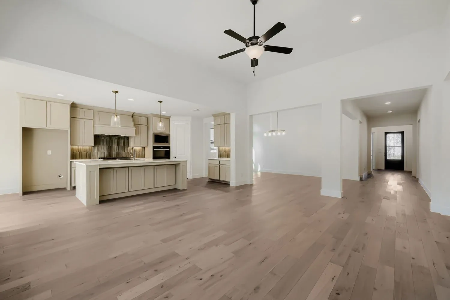 Vaulted ceiling with a ceiling fan, light wood-finish flooring, a kitchen island with pendant lighting, built-in oven, and a mosaic tile backsplash