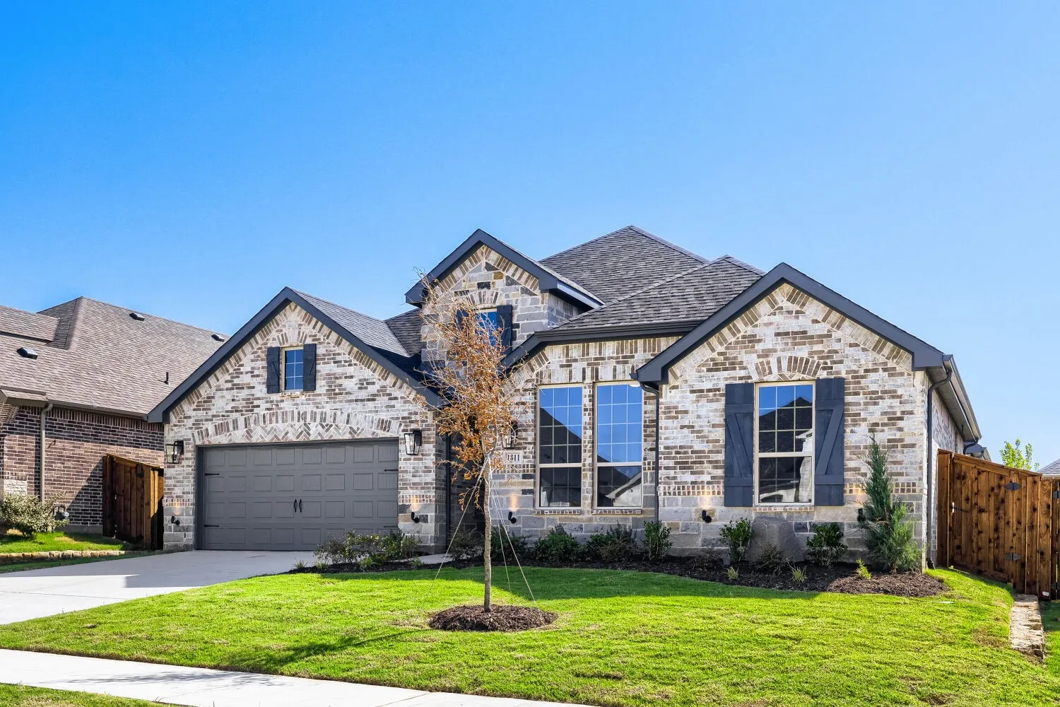 Brick and stone exterior with dark trim accents, a two-car garage, and established landscaping