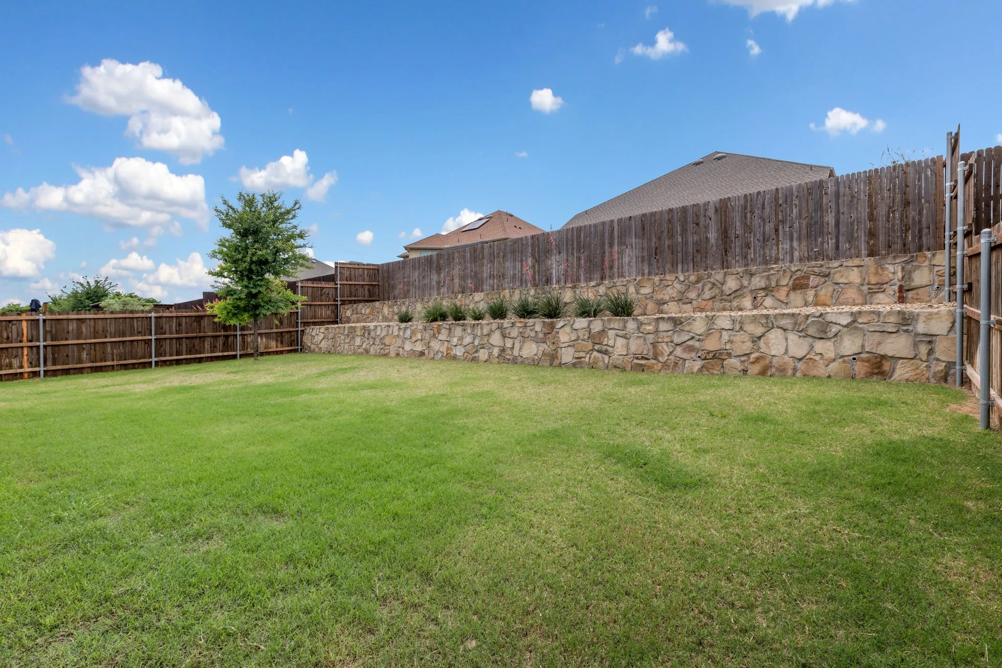 Expansive backyard featuring a lush lawn, tiered stone retaining walls, and planted greenery