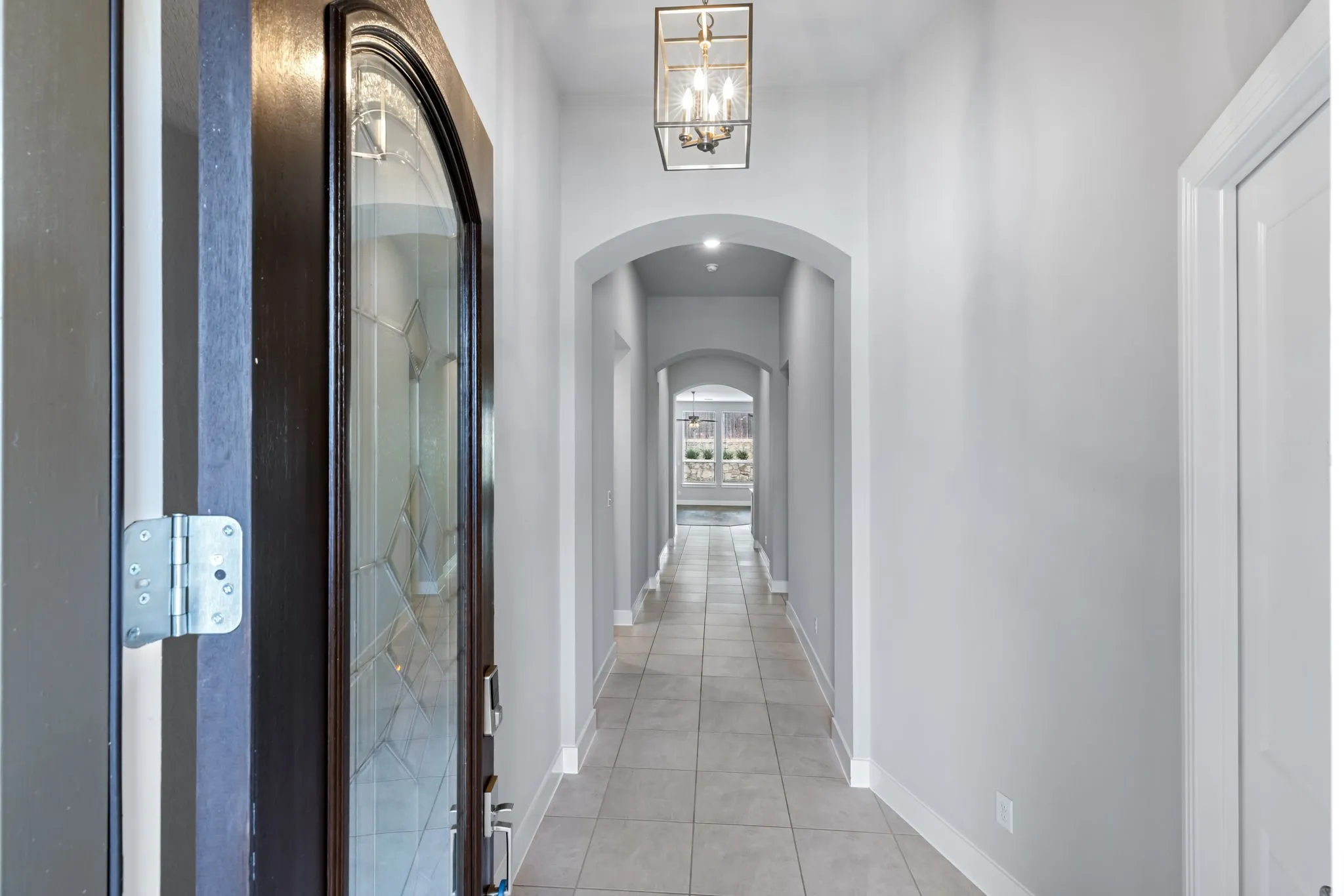 Entryway featuring a dark wood-finish door with decorative glass, tiled flooring, an overhead rectangular lantern-style light fixture, arched doorways, and light-colored walls