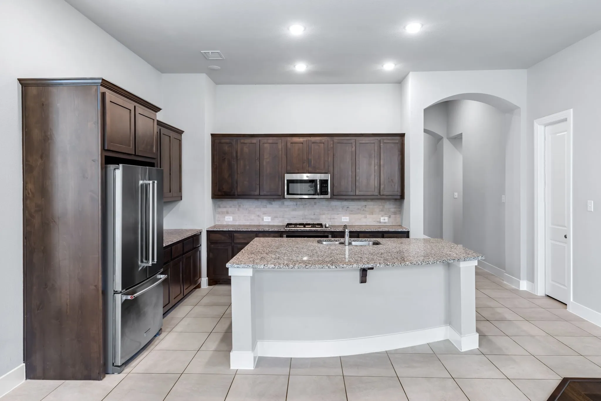 Contemporary kitchen featuring a spacious island with a built-in sink, granite countertops, and dark wood cabinetry