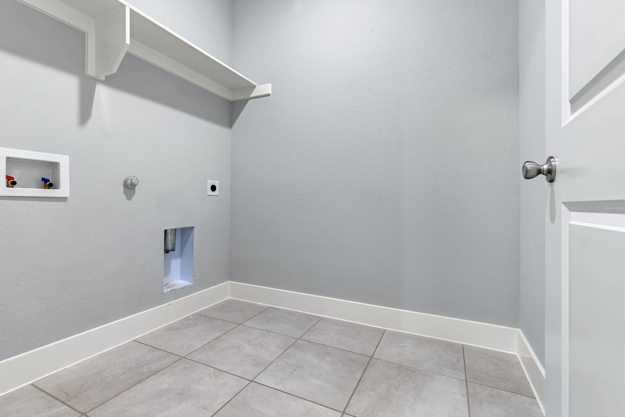 Dedicated utility area featuring a built-in shelf, grey tiled flooring, white baseboards, and a white paneled door with a brushed nickel knob