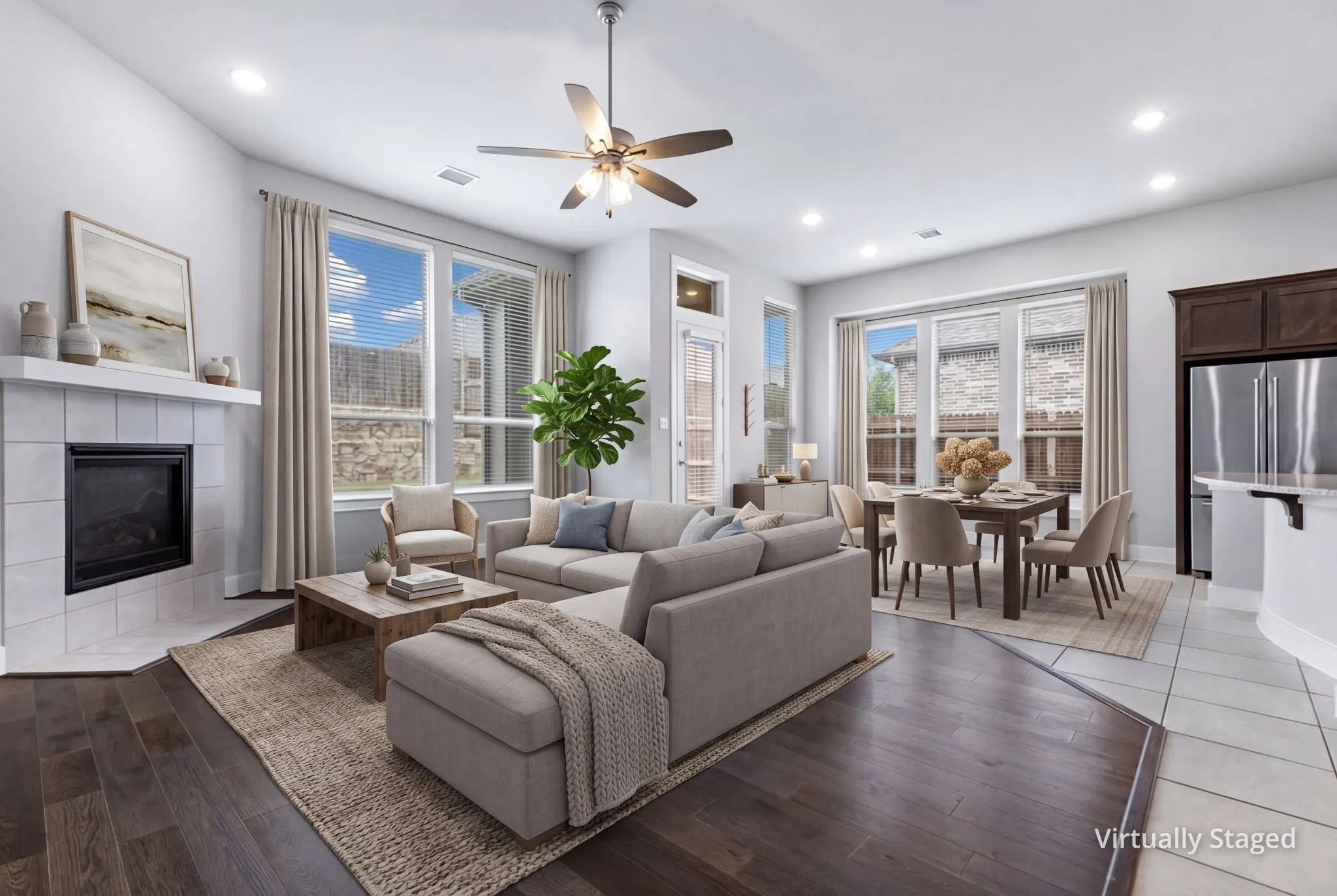 Expansive open-concept living area featuring a tile fireplace, high ceilings, dark wood-finish flooring, and abundant natural light from large windows