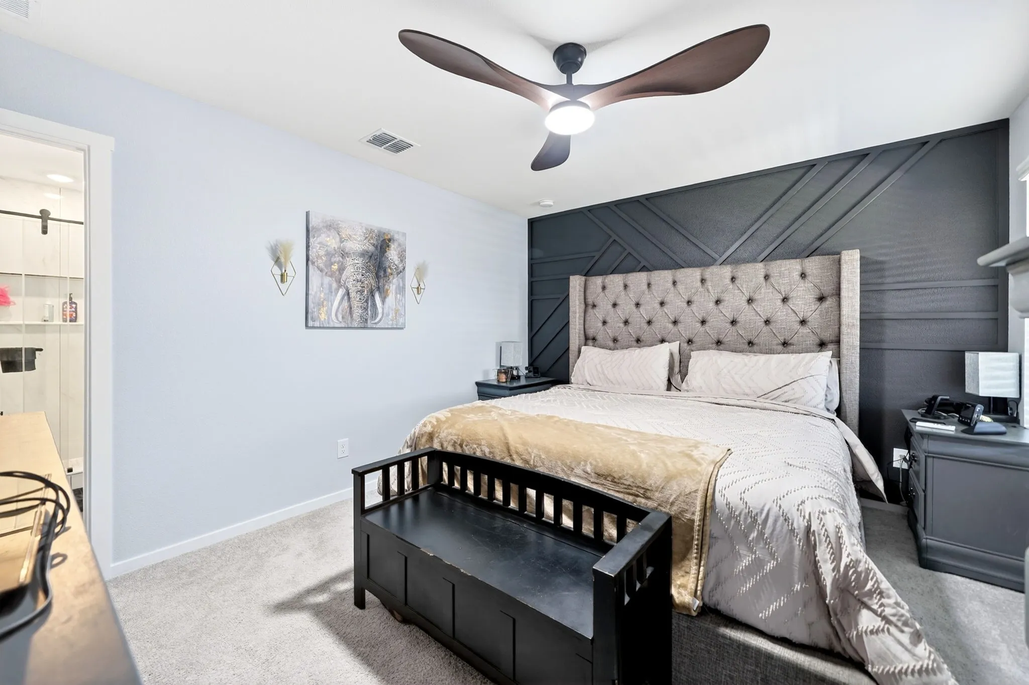 Bedroom featuring a dark accent wall with geometric molding, a ceiling fan with integrated lighting, and light-colored carpeting