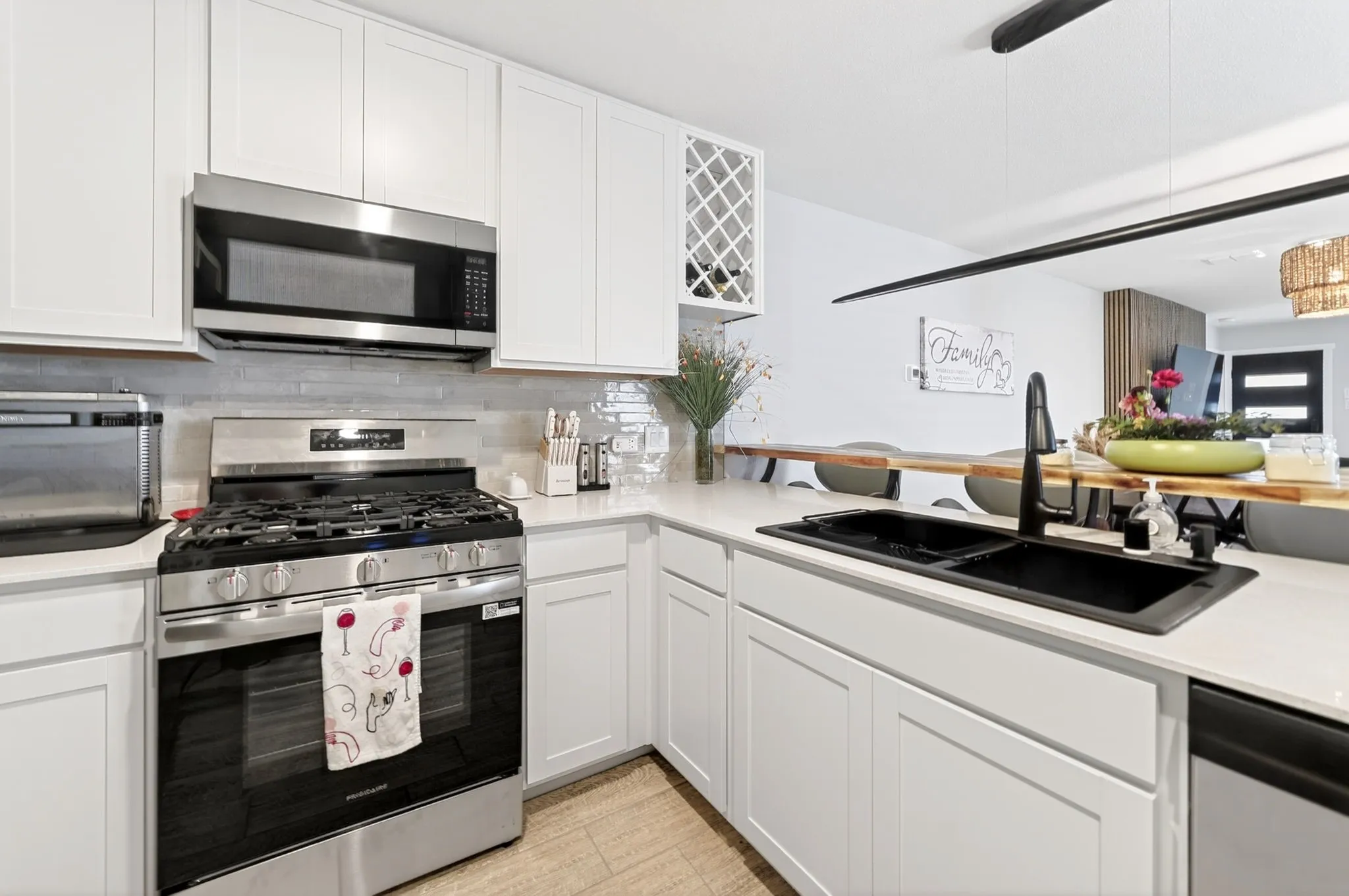 Modern kitchen featuring white shaker cabinetry, stainless steel appliances, a double basin sink with matte black faucet, light stone countertops, and a full-height tile backsplash
