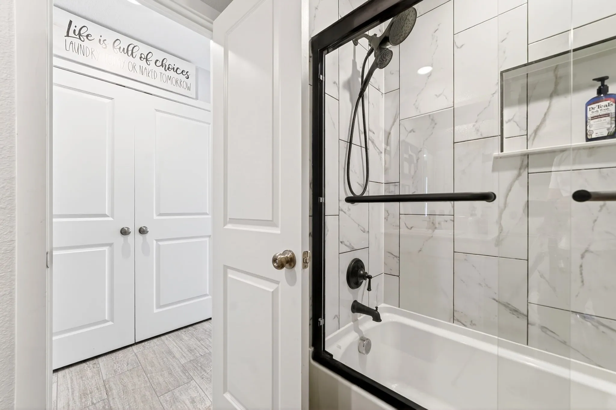 Bathtub with shower combination featuring a glass enclosure with black framing, black fixtures, and a recessed shelf within the tile surround