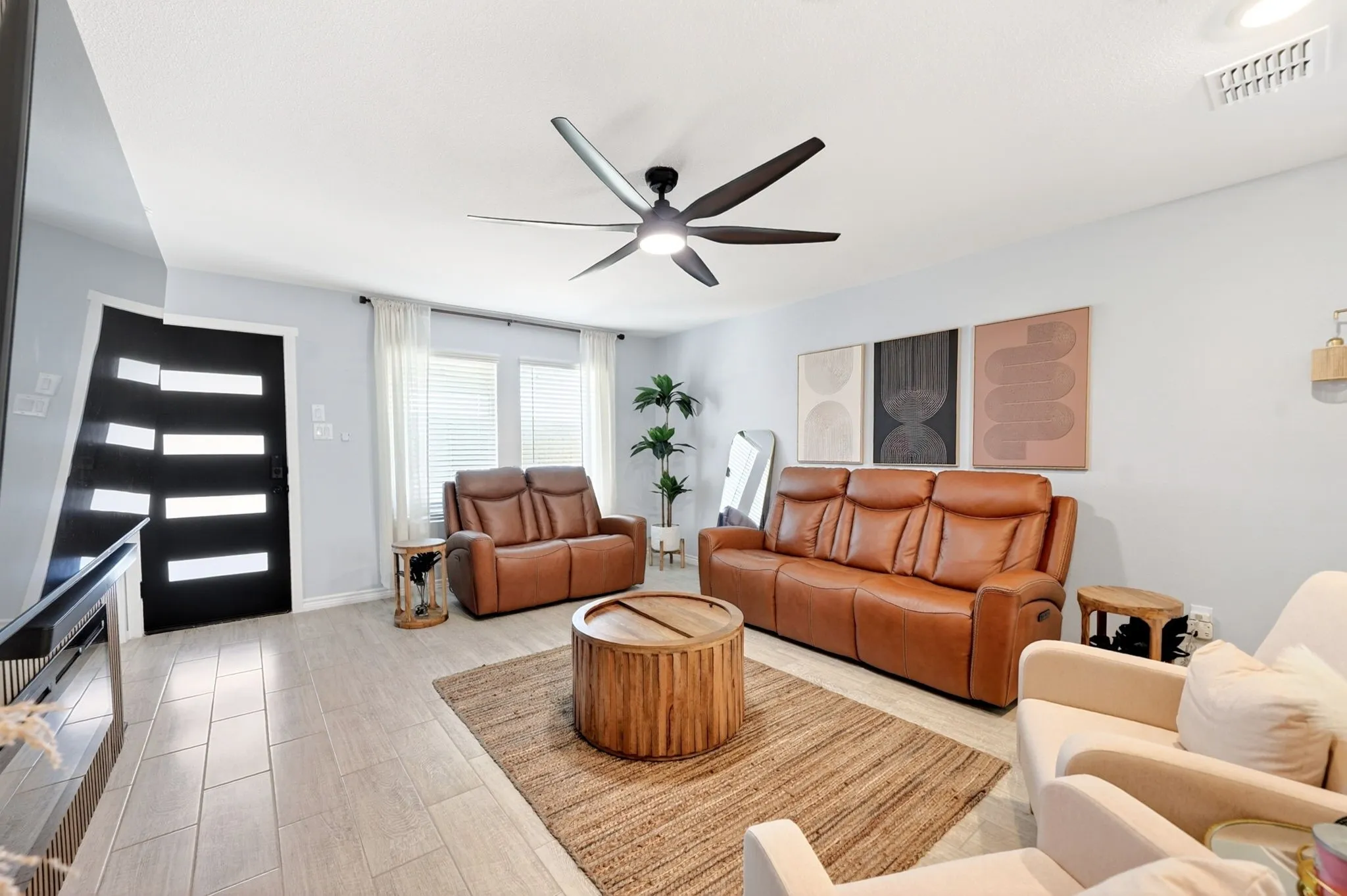 Spacious living area featuring light-toned tile flooring, light blue walls, and a contemporary ceiling fan