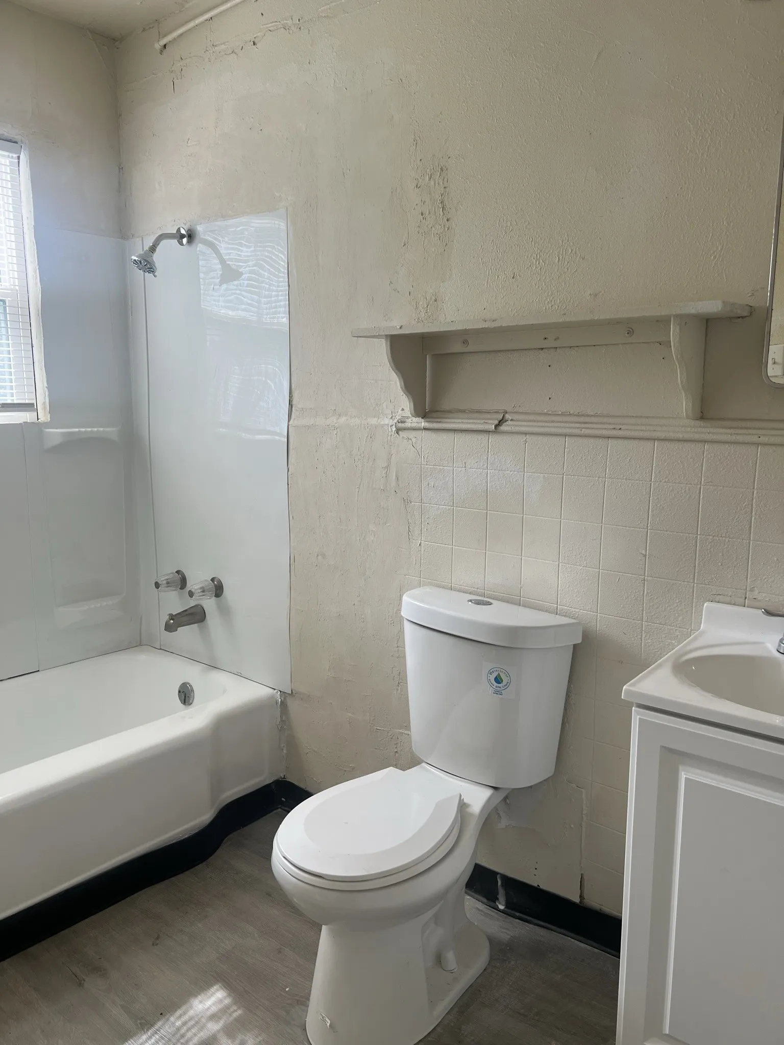 Bathroom featuring a white toilet, white vanity with integrated sink, white bathtub with shower, and wood-finish flooring