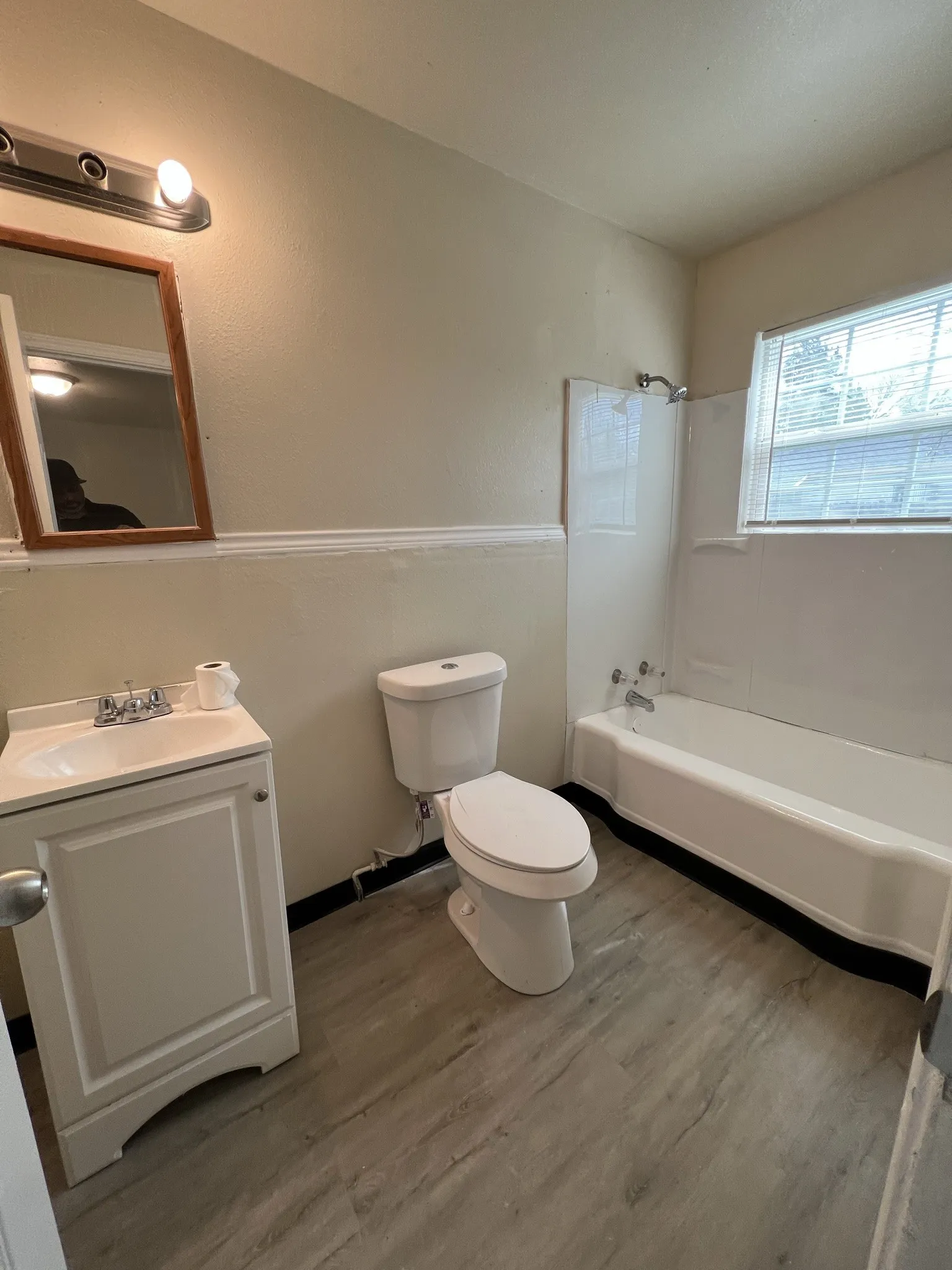 Bathroom featuring a white vanity with integrated sink, wood-finish flooring, and a full bathtub with shower surround
