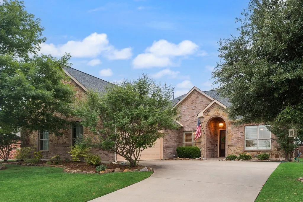 Brick residence featuring a covered arched entry, a two-car garage, and established landscaping