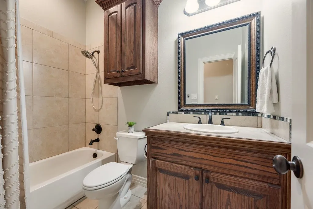 Bathroom featuring a bathtub with tile surround, dark wood vanity with white countertop, framed mirror, and a wall-mounted cabinet