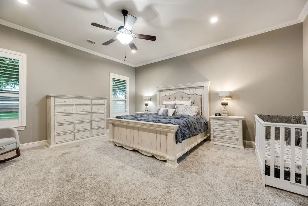Primary Suite is fully Carpeted, featuring neutral wall tones, white crown molding, recessed lighting, and a ceiling fan with integrated light & Fireplace