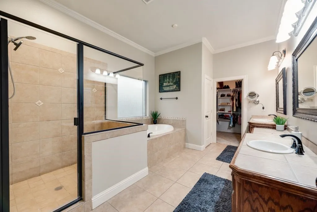 Spacious primary bathroom featuring a glass-enclosed shower with tile surround, a built-in soaking tub, dual vanity with tile countertops and integrated sinks, and a luxurious walk-in closet