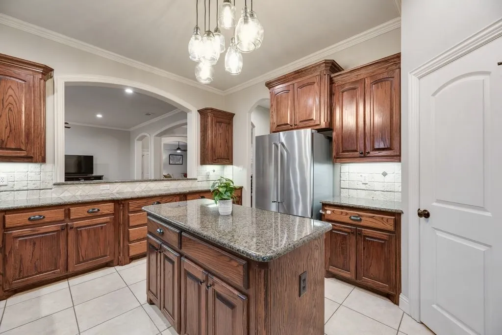 Kitchen featuring wood cabinetry, granite countertops, tile flooring, a central island, and stainless steel appliances
