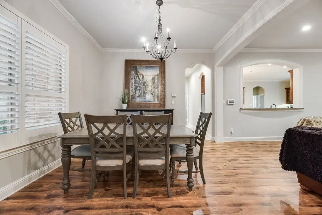Dining area featuring wood-finish flooring, plantation shutters, crown molding, an arched pass-through, and an arched entryway