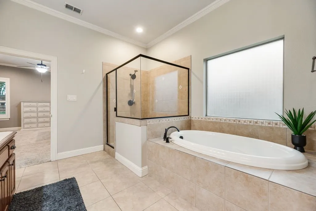 Spacious primary bathroom featuring an oval soaking tub, a clear glass shower enclosure with dark framing, and ceramic tile flooring
