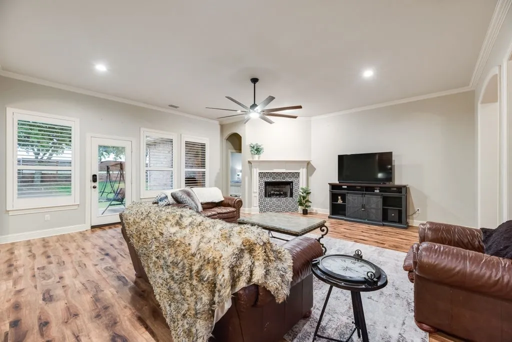 Living area featuring wood-finish flooring, recessed lighting, oversized ceiling fan, and crown molding, classically tiled fireplace is a focal point