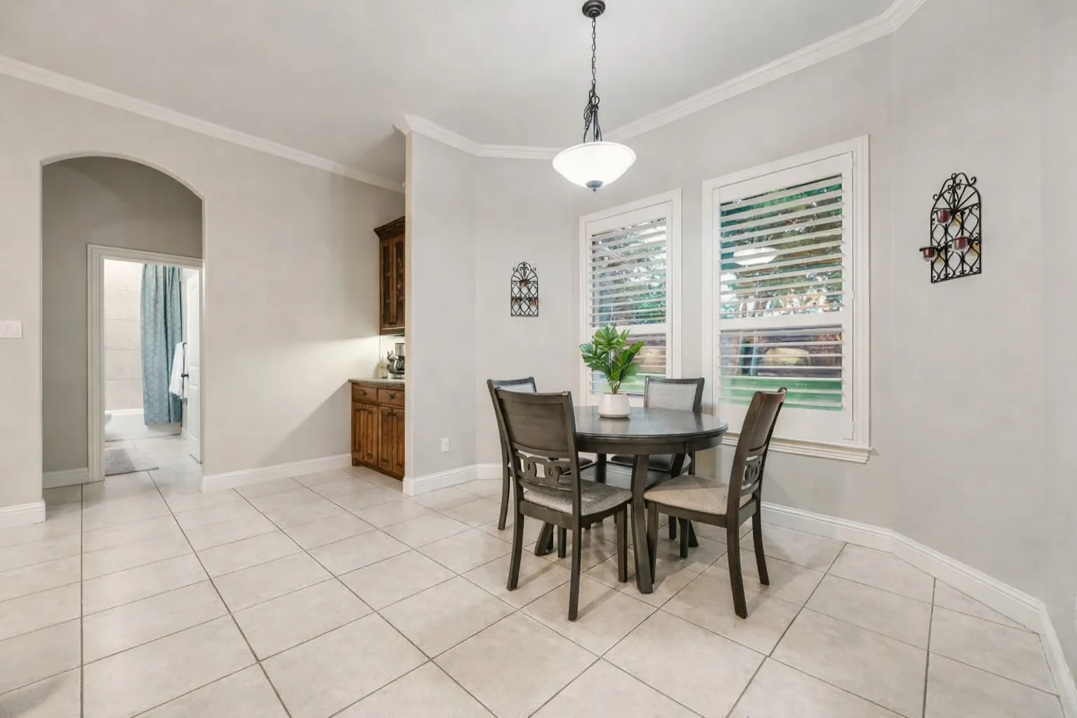 Casual dining area featuring neutral tile flooring, two large windows with plantation shutters, a built-in cabinetry unit, and an arched entryway