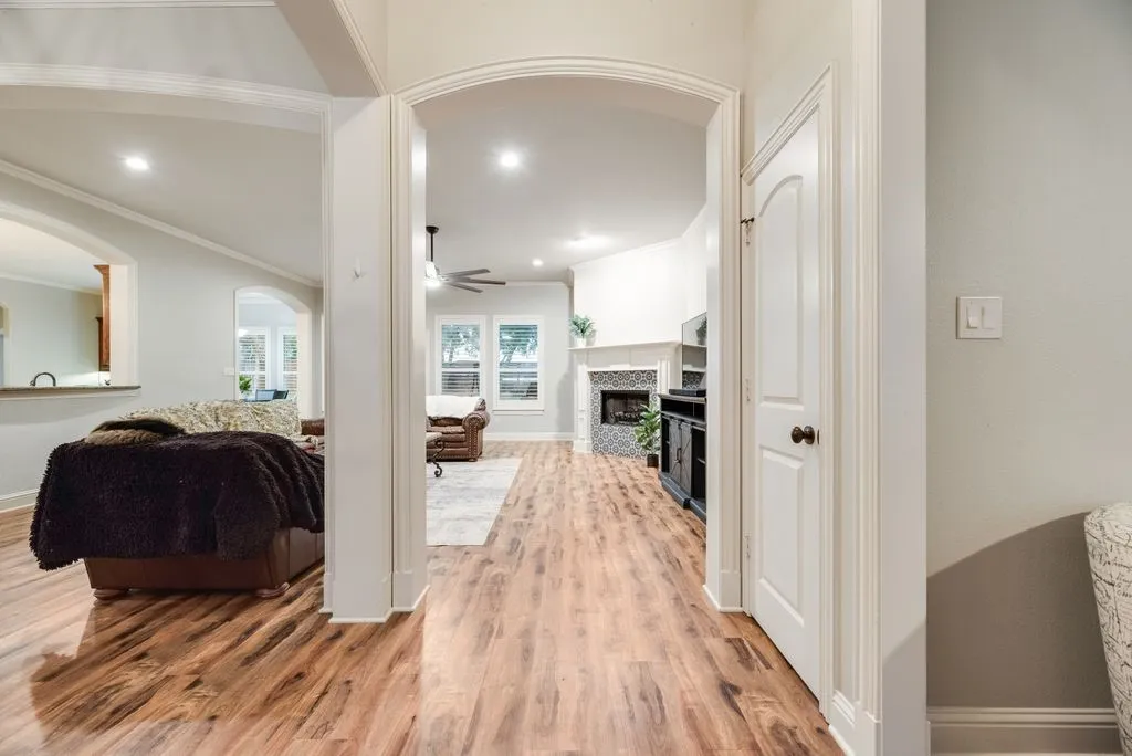 View from the entry, Wood-finish flooring throughout, arched doorways, a fireplace with a decorative tile surround, recessed lighting, and white baseboards