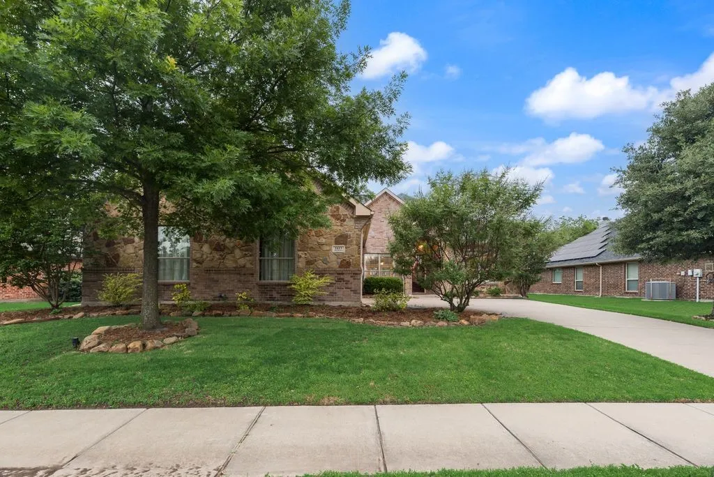 brick residence with a well-maintained lawn, mature trees, and a concrete driveway
