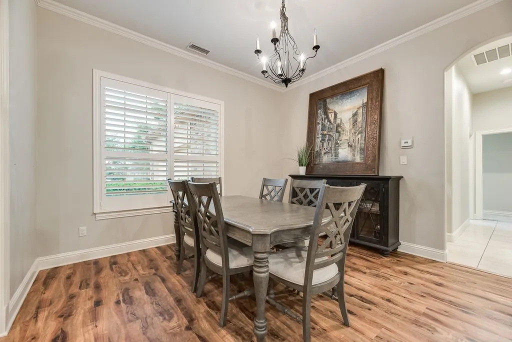 Dining area featuring wood-finish flooring, white plantation shutters, crown molding, and a chandelier with candelabra bulbs
