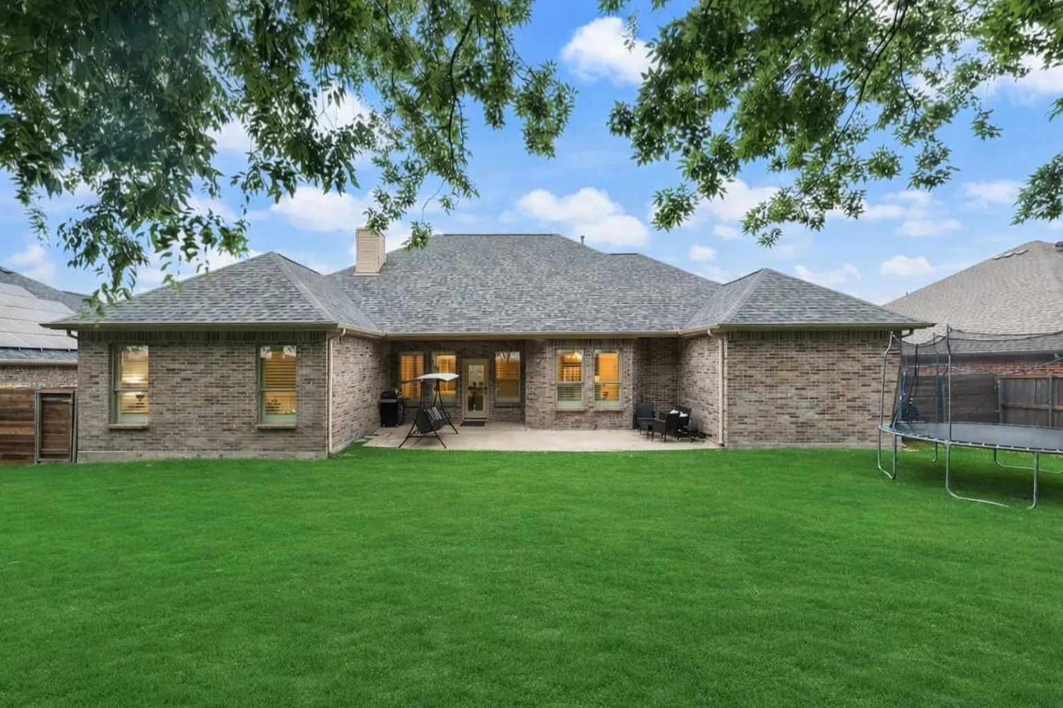 Expansive green lawn backing a brick exterior with a rear patio