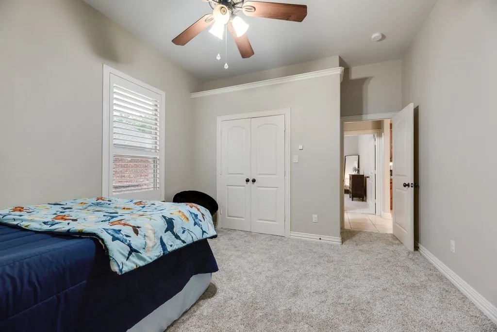 Bedroom 2: Carpeted room featuring a ceiling fan with light fixture, white plantation shutters, vaulted ceiling, and white paneled doors with black hardware