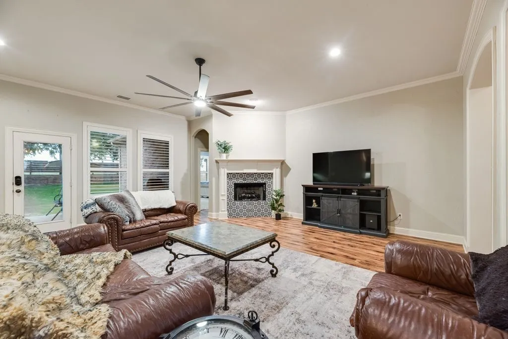 Living area featuring wood-finish flooring, a decorative fireplace with tile surround, a large ceiling fan, recessed lighting, and crown molding
