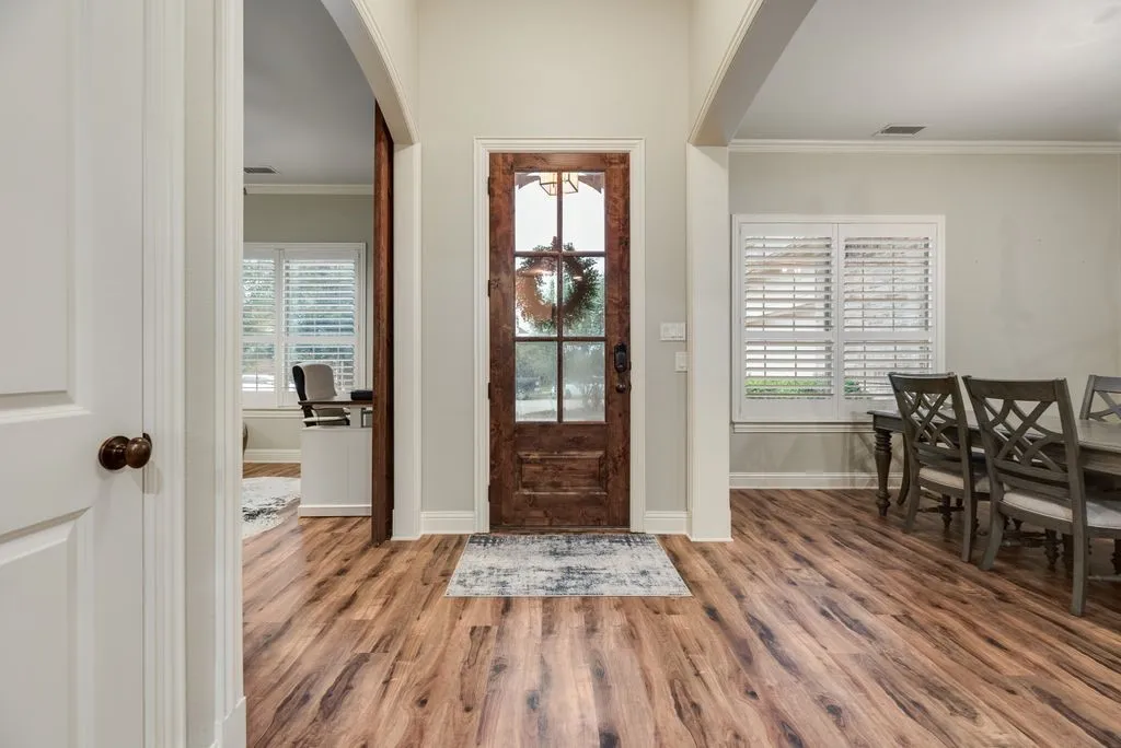 Entryway featuring wood-finish flooring, a wood-panel door with glass inserts, and white plantation shutters