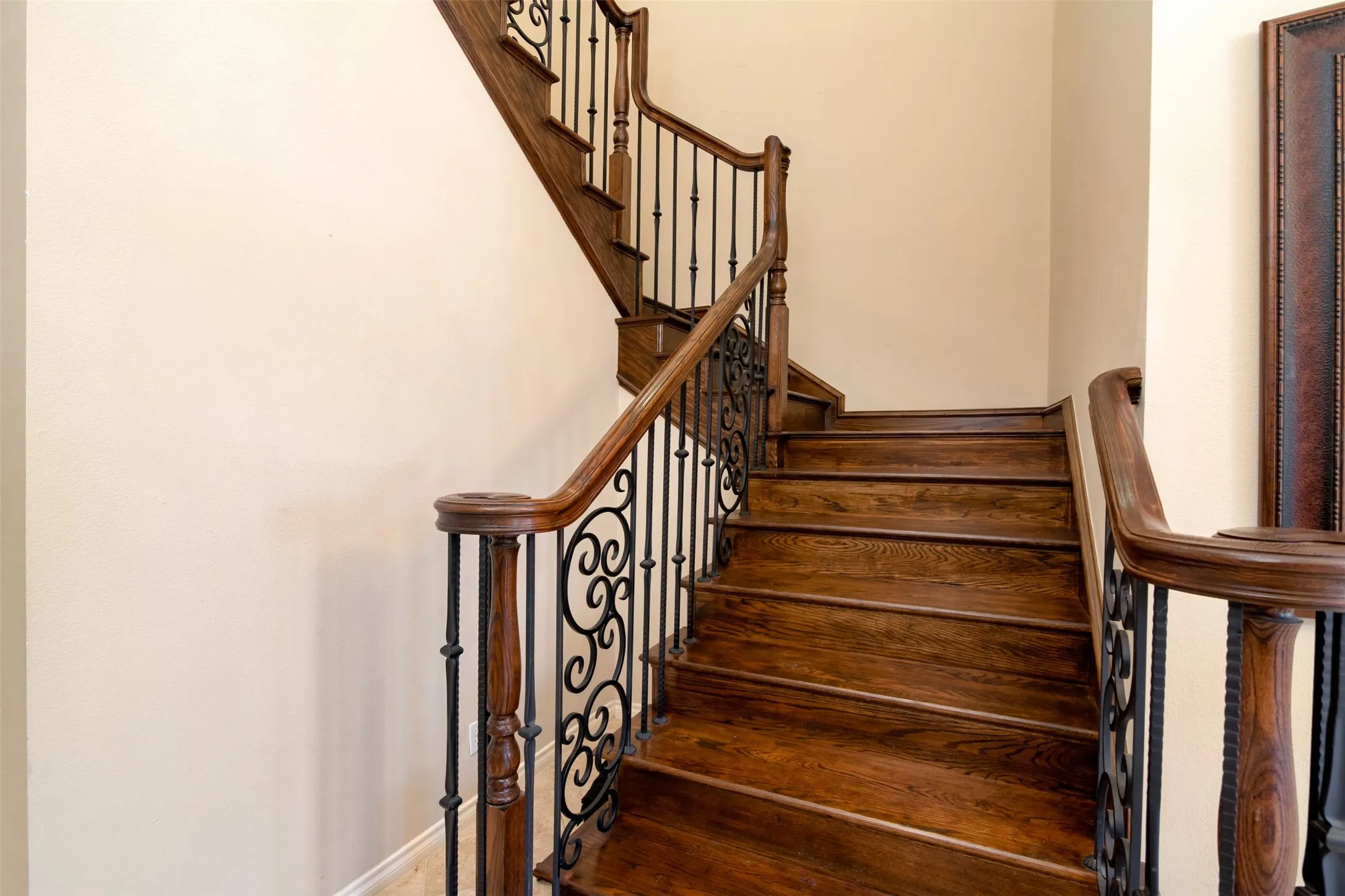 Curved wood staircase featuring wrought iron balusters with ornate scrollwork and a substantial wood handrail