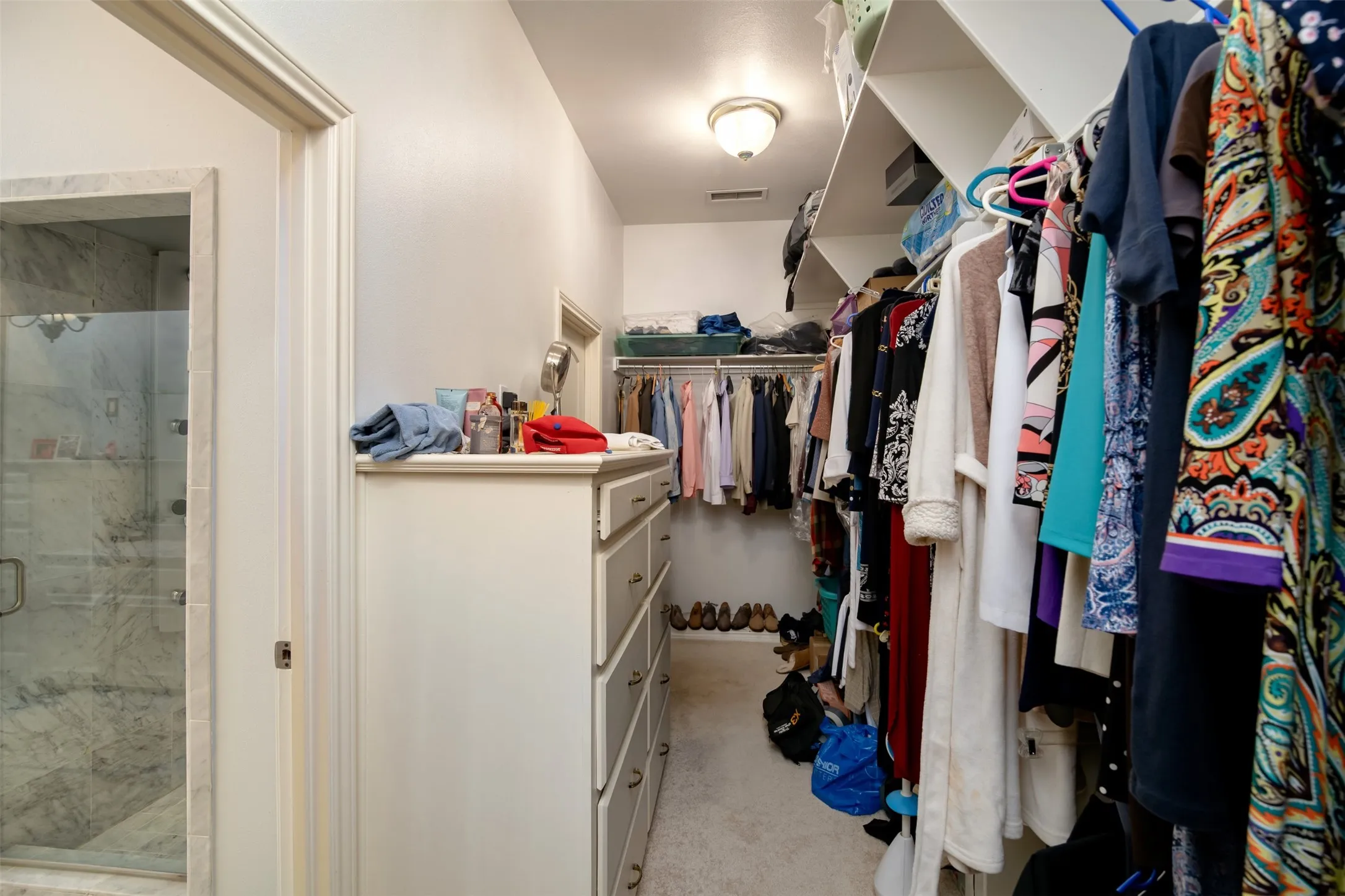 Walk-in closet featuring extensive built-in shelving, multiple hanging rods, and a multi-drawer dresser unit