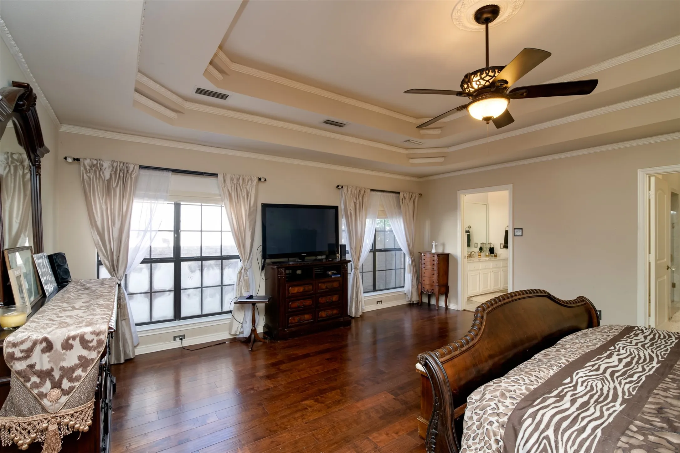 Spacious interior room featuring wood-finish flooring, decorative tray ceiling, and an ornate ceiling fan