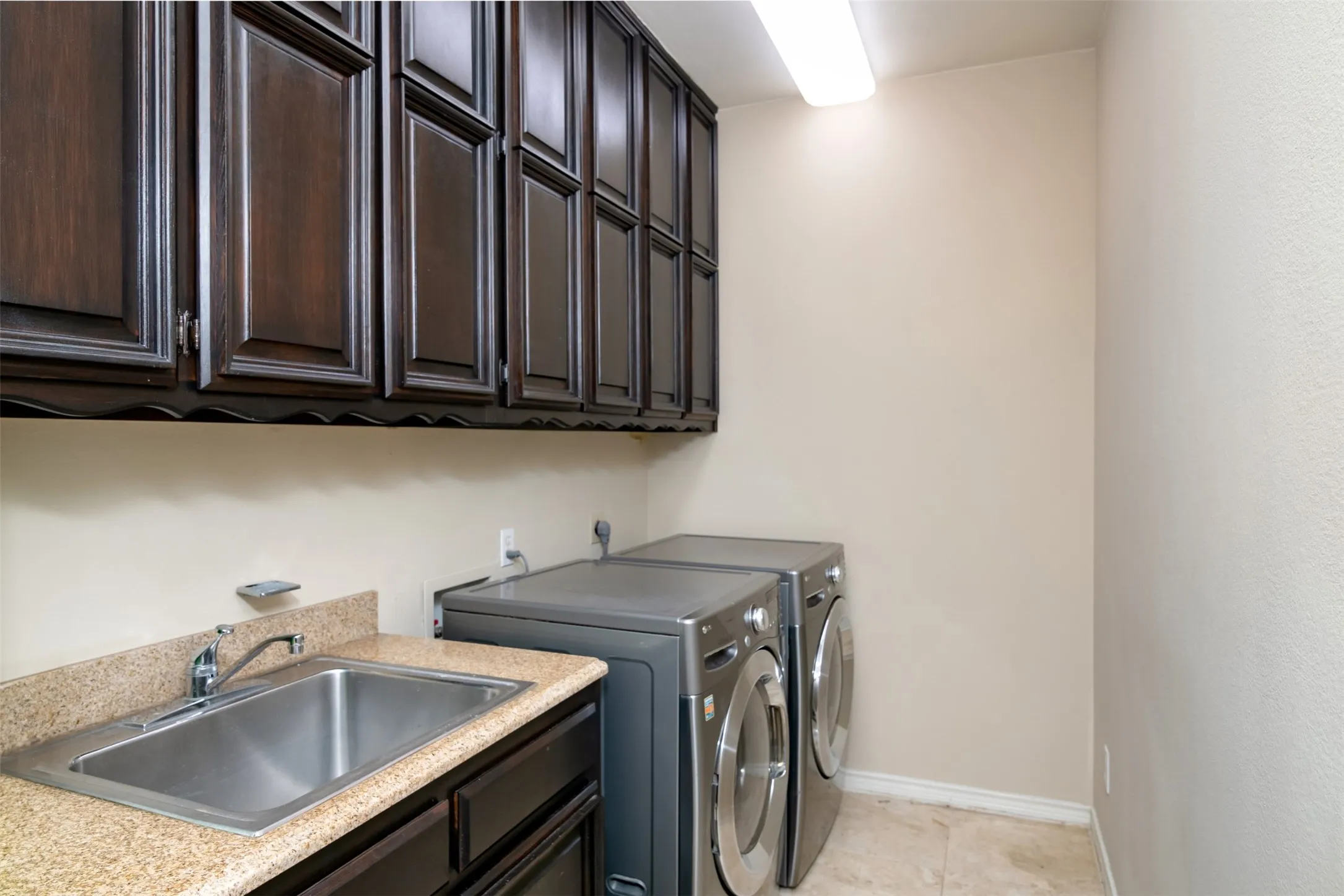 Utility area featuring dark wood-finish cabinetry, a stainless steel sink with a chrome faucet, a speckled countertop, and neutral wall paint