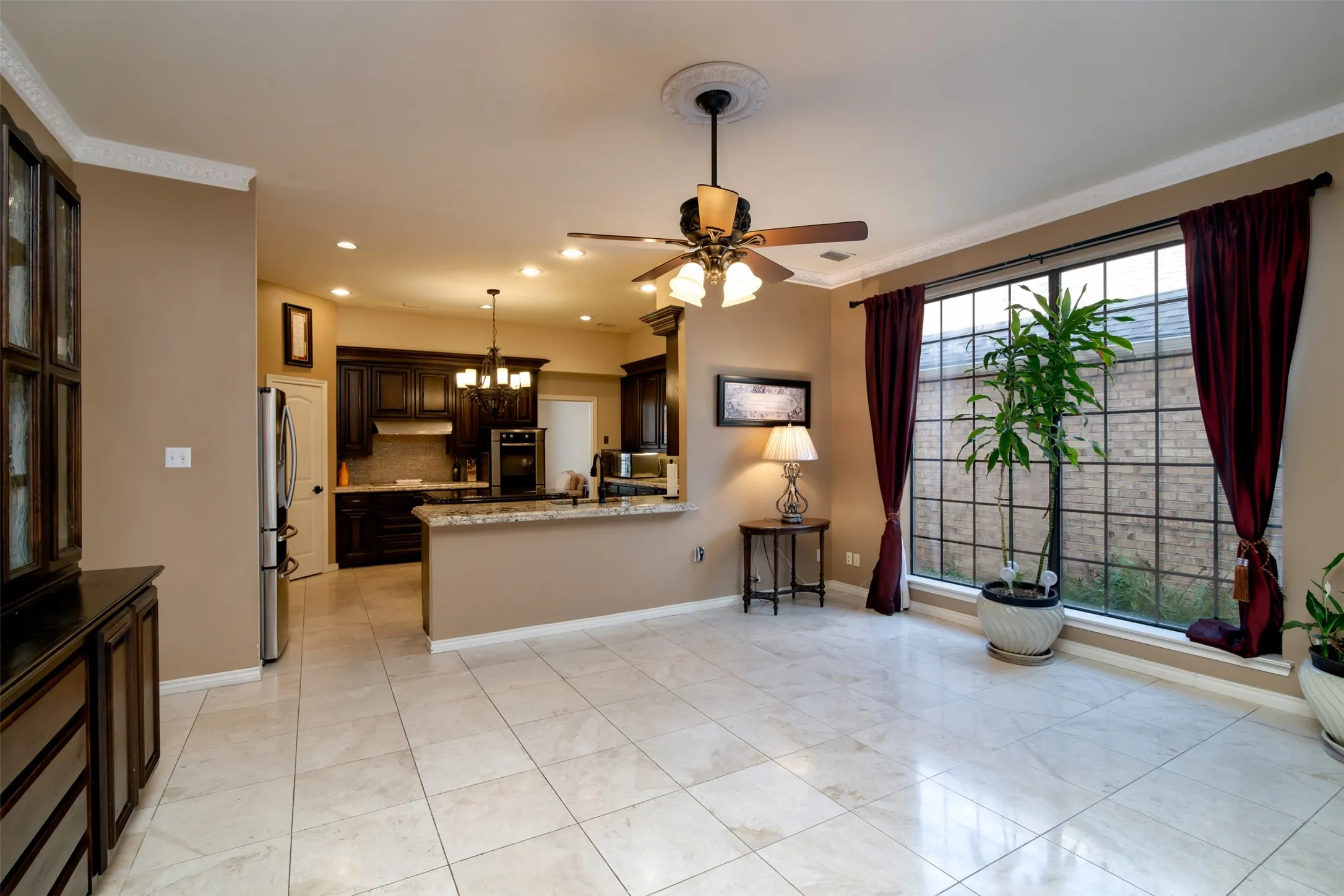 Open-concept living area featuring light-toned large format tile flooring, a multi-pane grid window, and a ceiling fan with integrated lighting