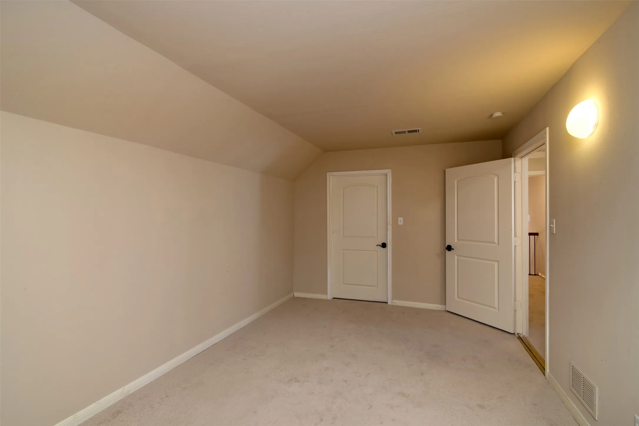 Carpeted room featuring a sloped ceiling, light-colored walls, and two paneled doors with dark hardware