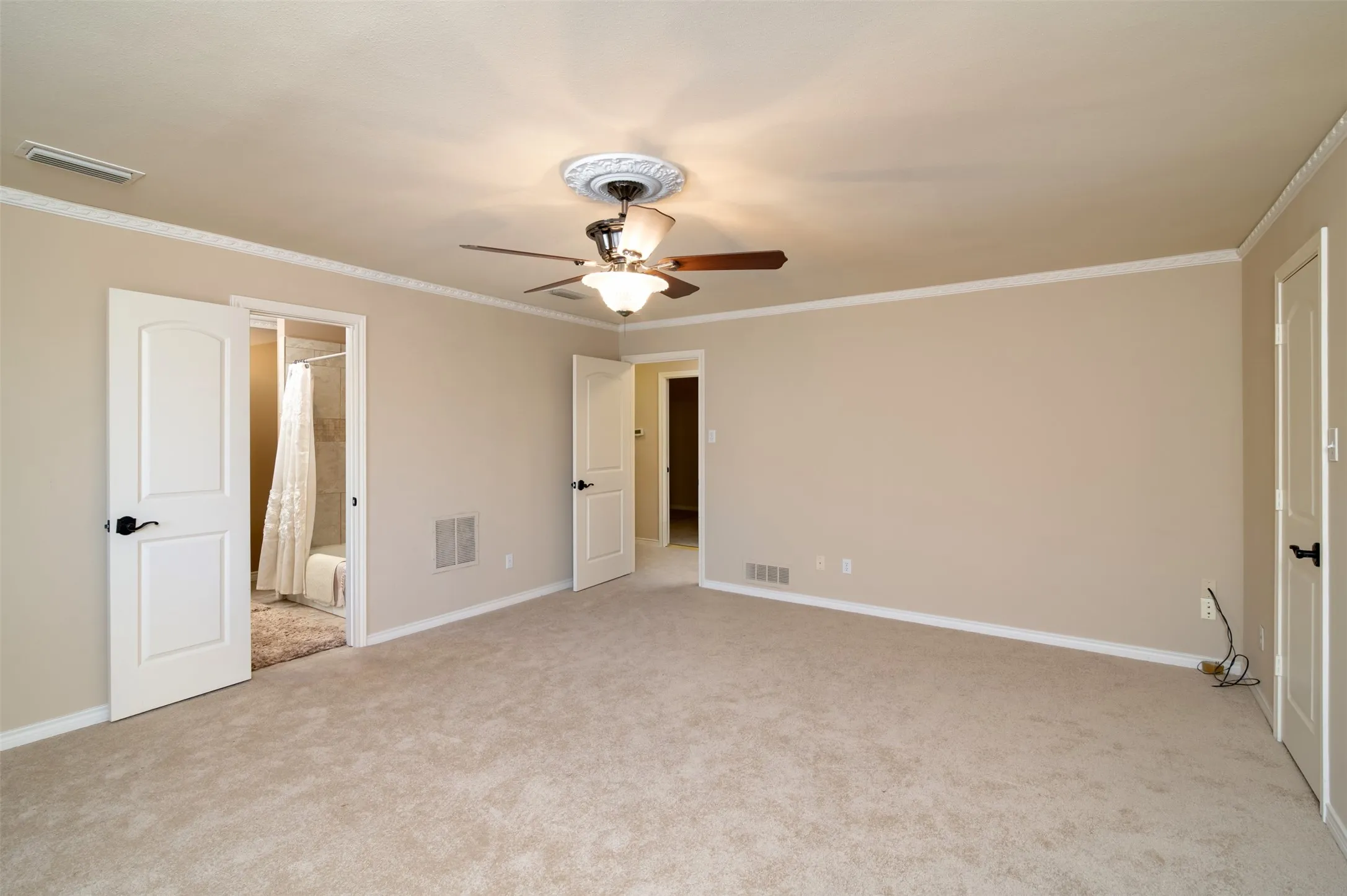 Spacious carpeted room featuring crown molding, a ceiling fan with light fixture, and two panel doors with black hardware