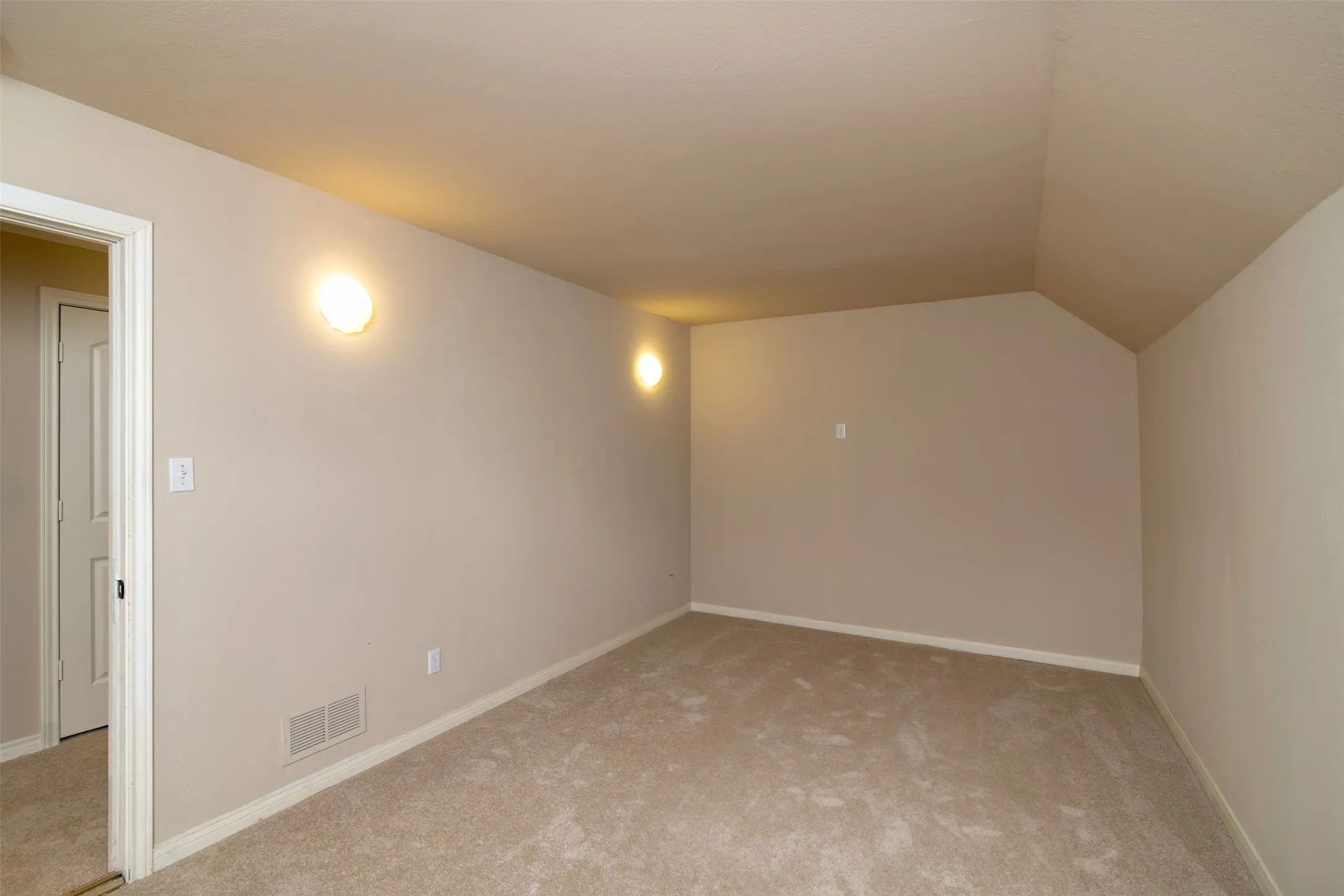 Carpeted room with neutral wall tones and a vaulted ceiling feature