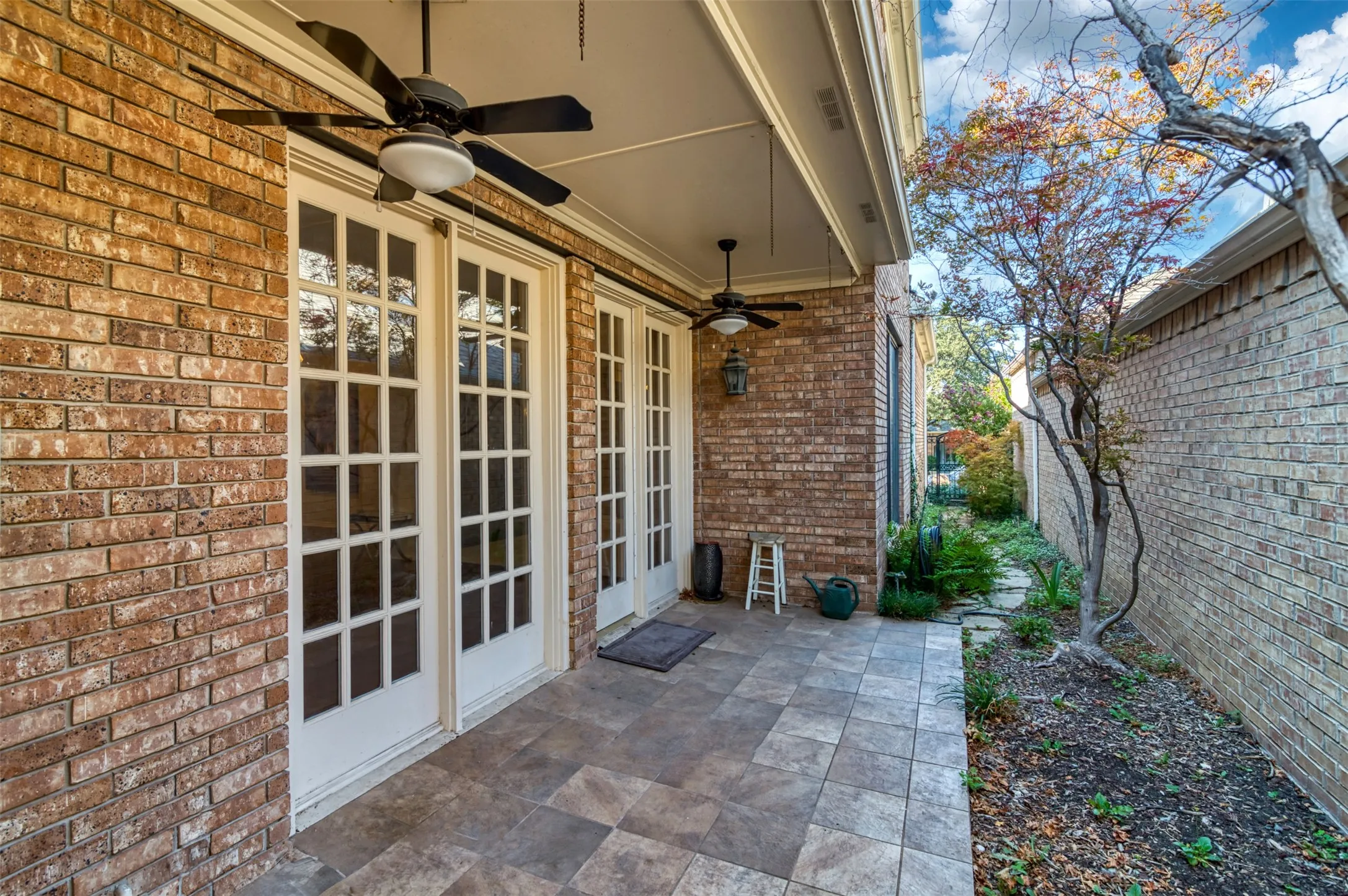 Covered patio featuring two sets of French doors, brick exterior, ceiling fans, and tiled flooring
