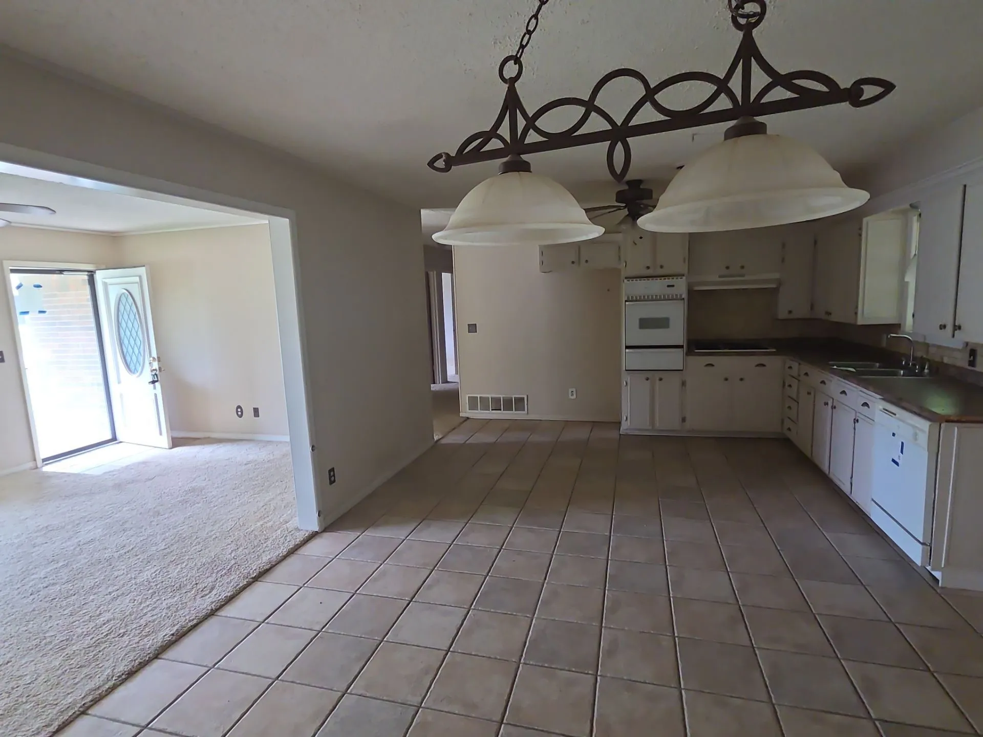 Kitchen and dining area featuring tile flooring, white cabinetry, integrated oven, and a double basin sink