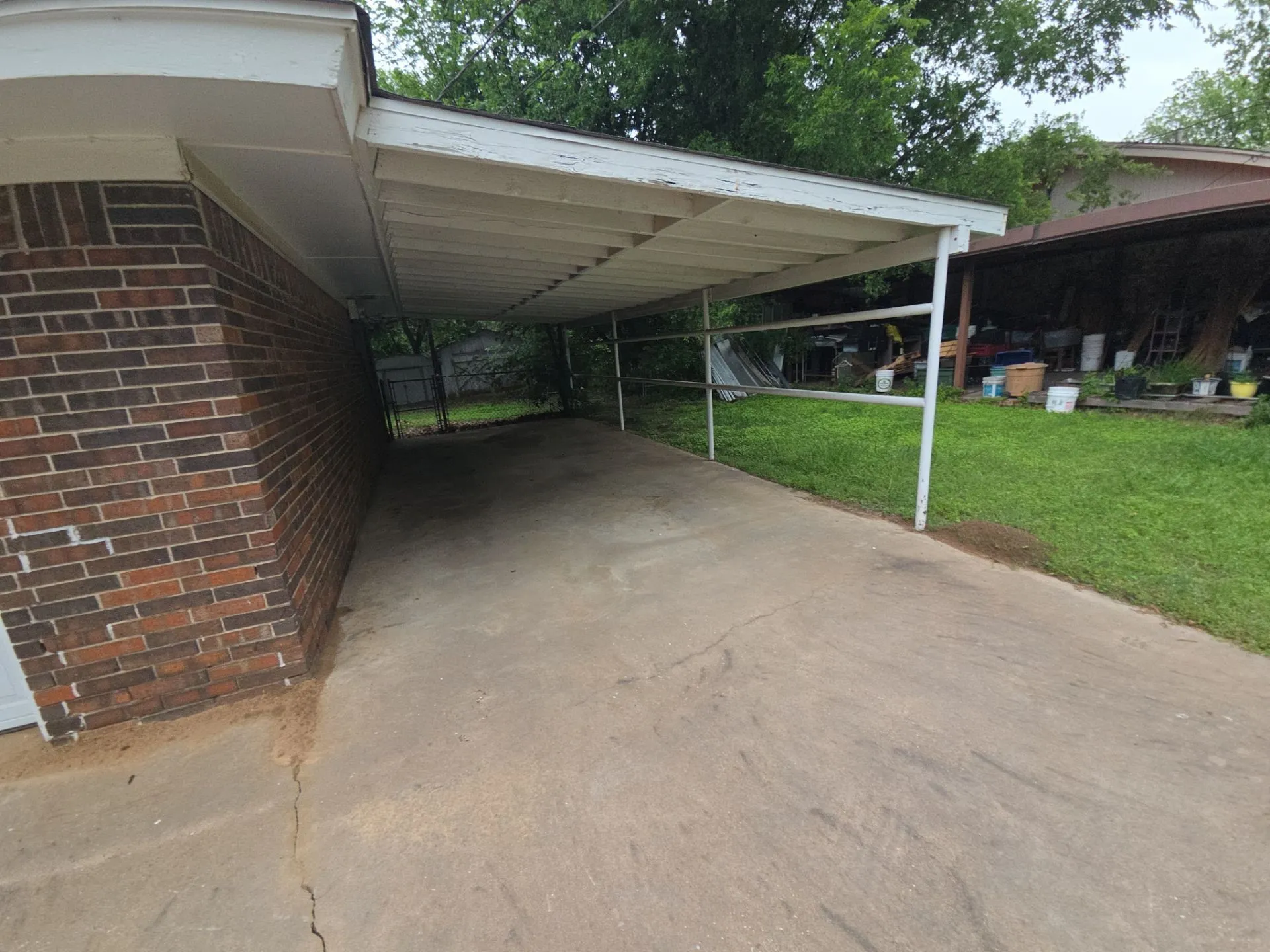 Carport providing covered parking, featuring a concrete driveway and brick exterior wall