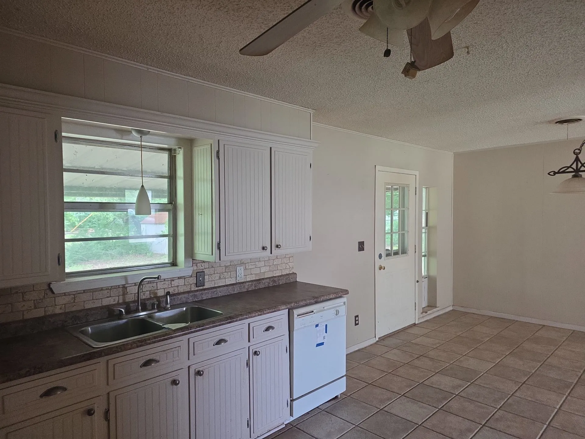 Kitchen area featuring beadboard cabinetry with brushed nickel hardware, a double basin stainless steel sink, a tiled backsplash, and a dishwasher