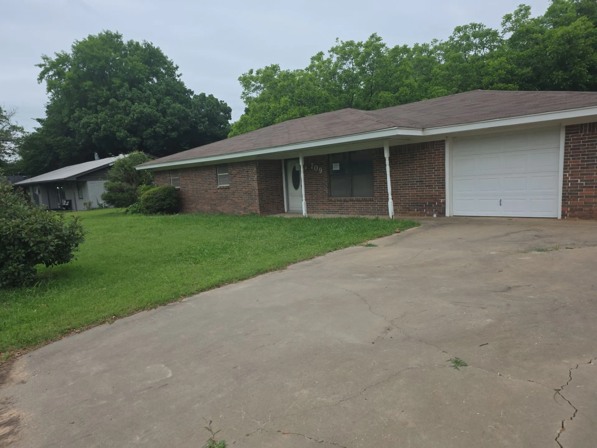 Brick exterior residence featuring a white paneled garage door, a front porch with white support columns, and a concrete driveway