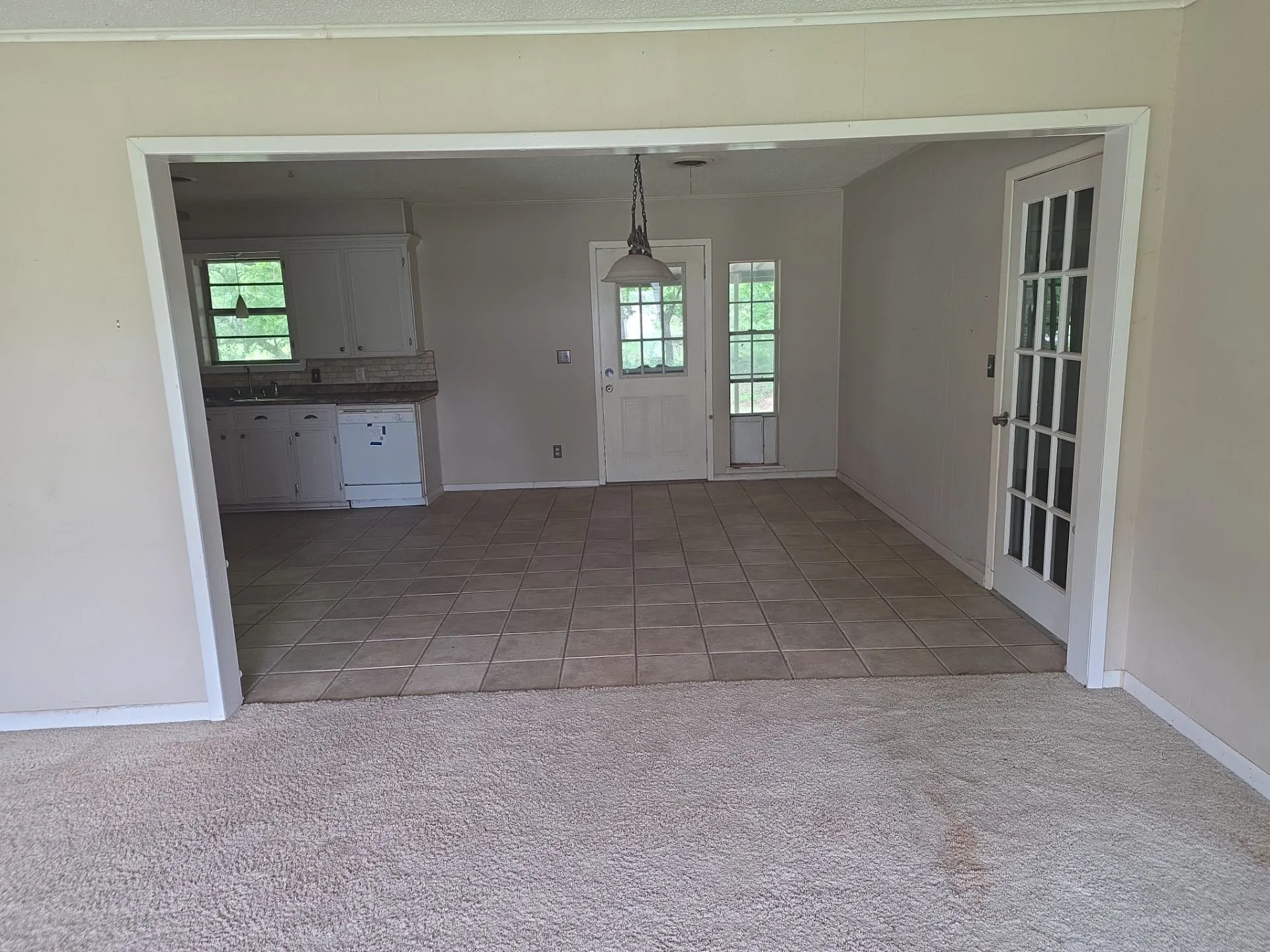Open concept living area featuring light-toned carpeting and an expansive entryway to a tiled dining space