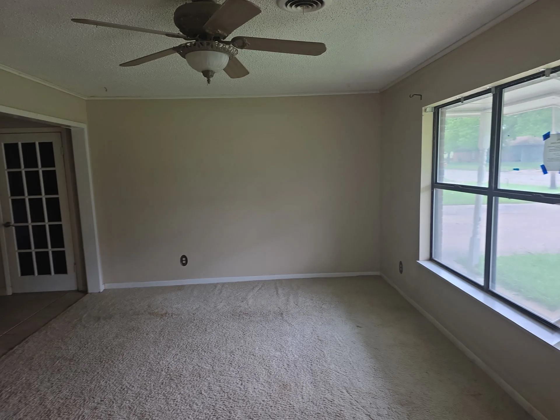 Carpeted room featuring a ceiling fan with integrated lighting, a large window with white trim, and a French door with multiple glass panes