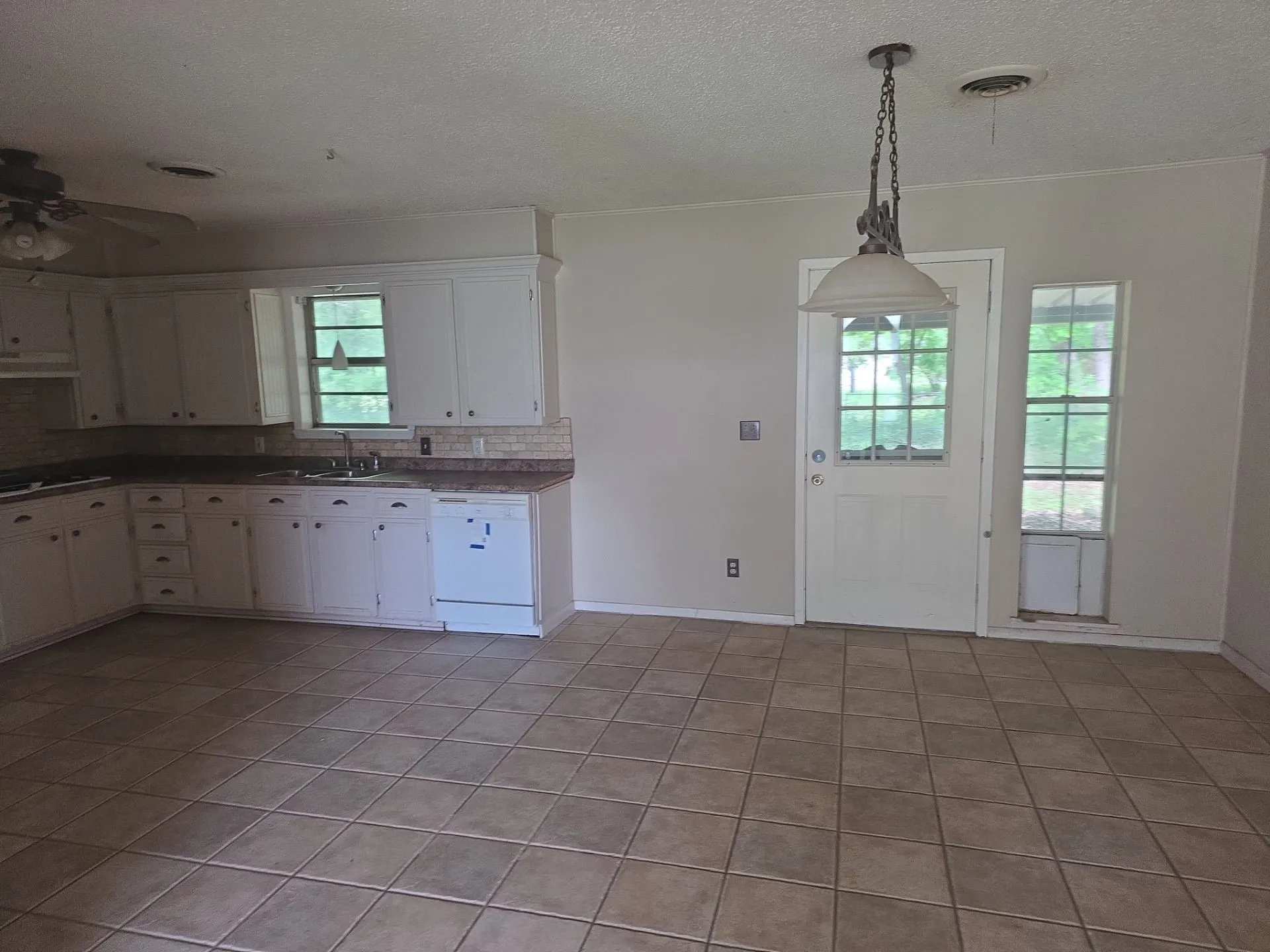 Tile flooring extending throughout this area, offering a functional kitchen space with white cabinetry and a white dishwasher