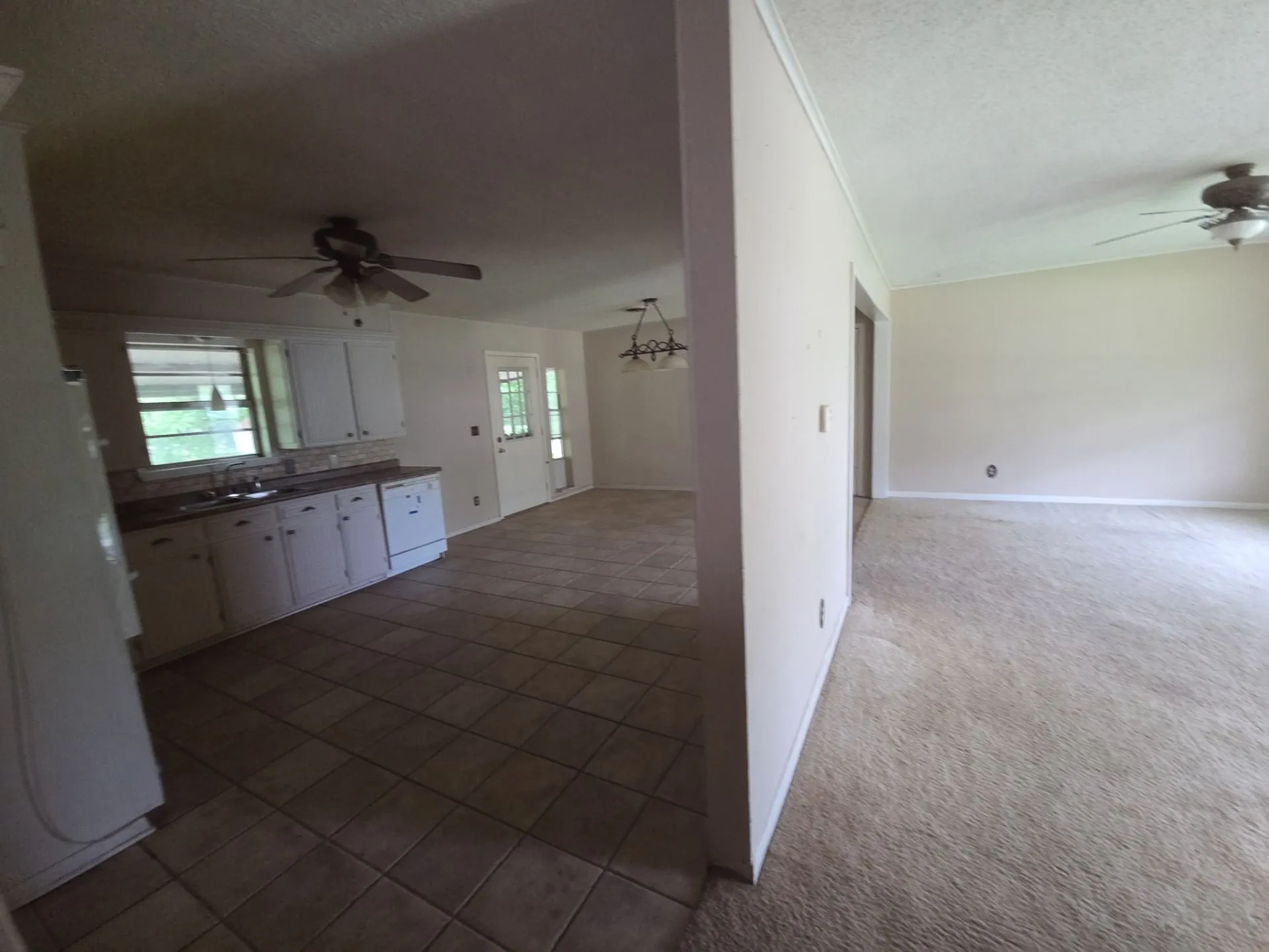 Kitchen and living area featuring a tile floor in the kitchen, white cabinetry, a dishwasher, and a window above the sink