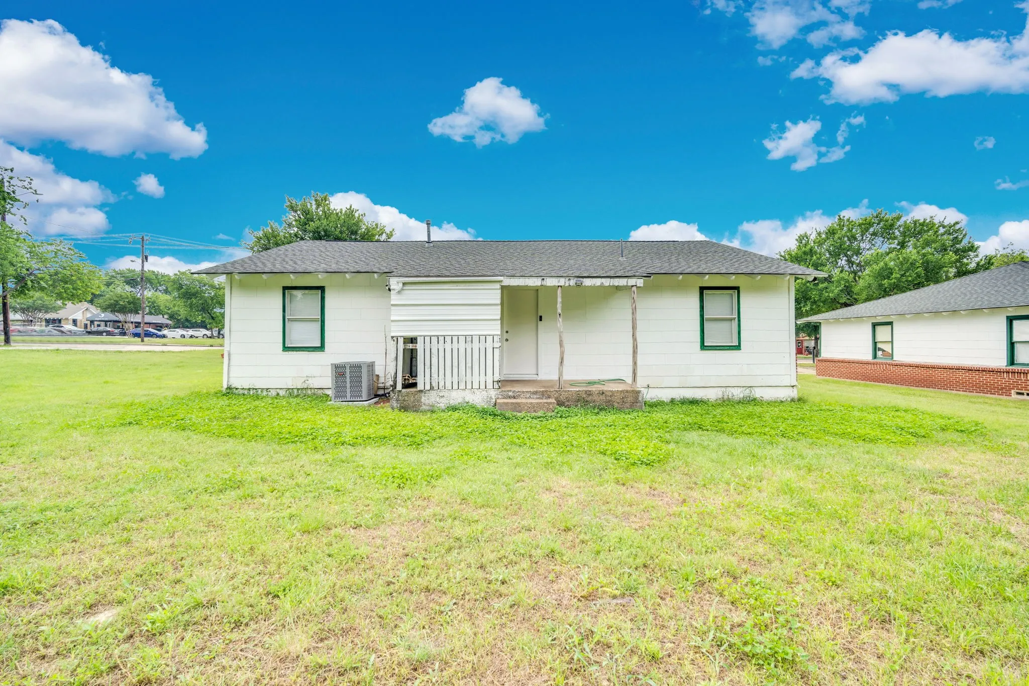 White exterior featuring green trim windows, a covered porch, and a visible HVAC unit