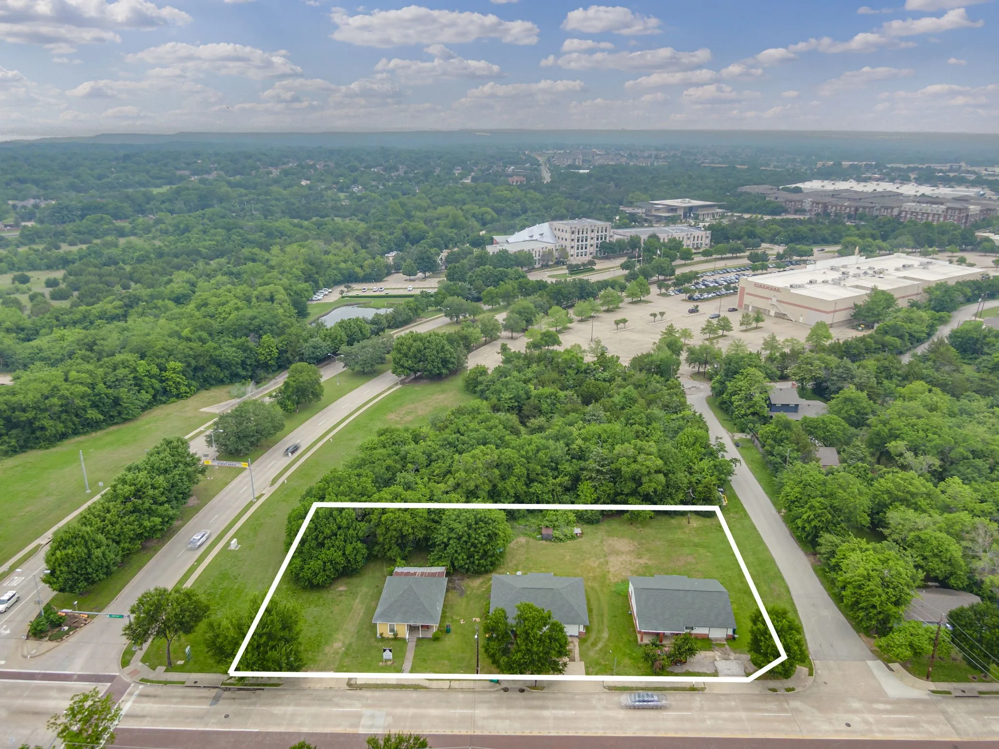 Expansive land parcel featuring three existing structures, mature trees, and a concrete street frontage