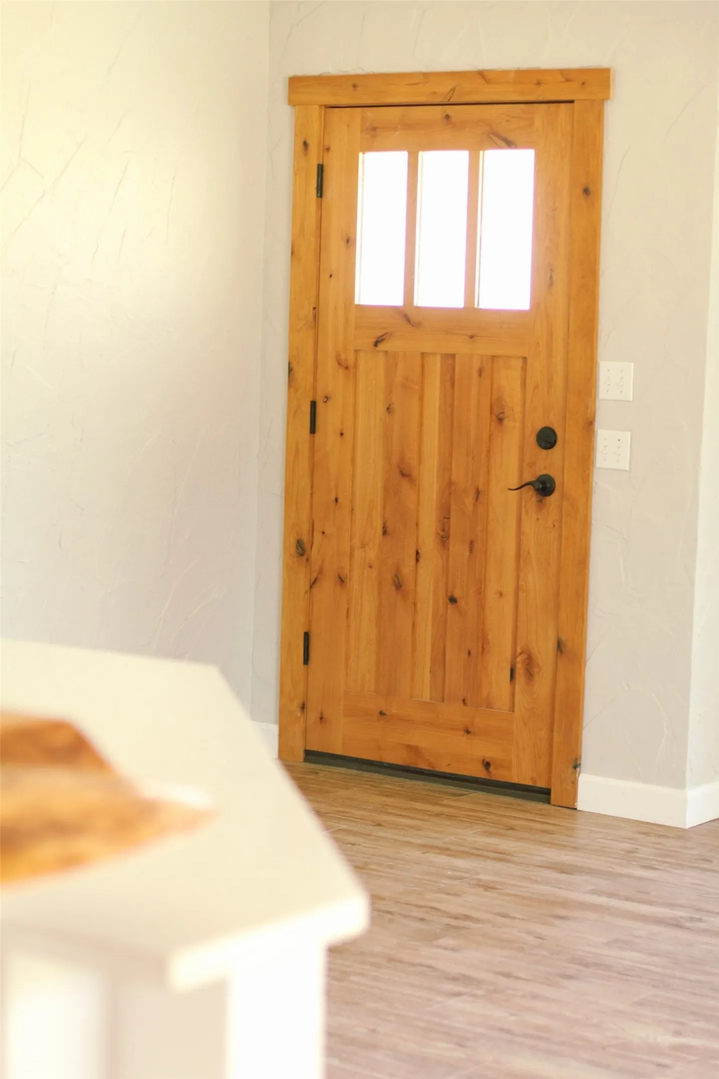 Solid wood entry door with vertical paneling, three glass lites, and matte black hardware