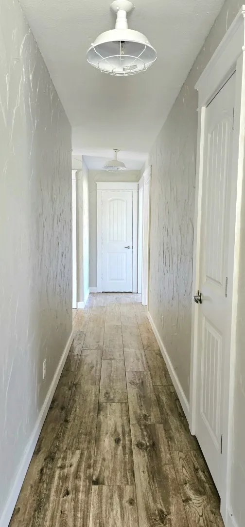 Hallway featuring wood-finish flooring, white baseboards, textured walls, and industrial-style flush-mount lighting fixtures